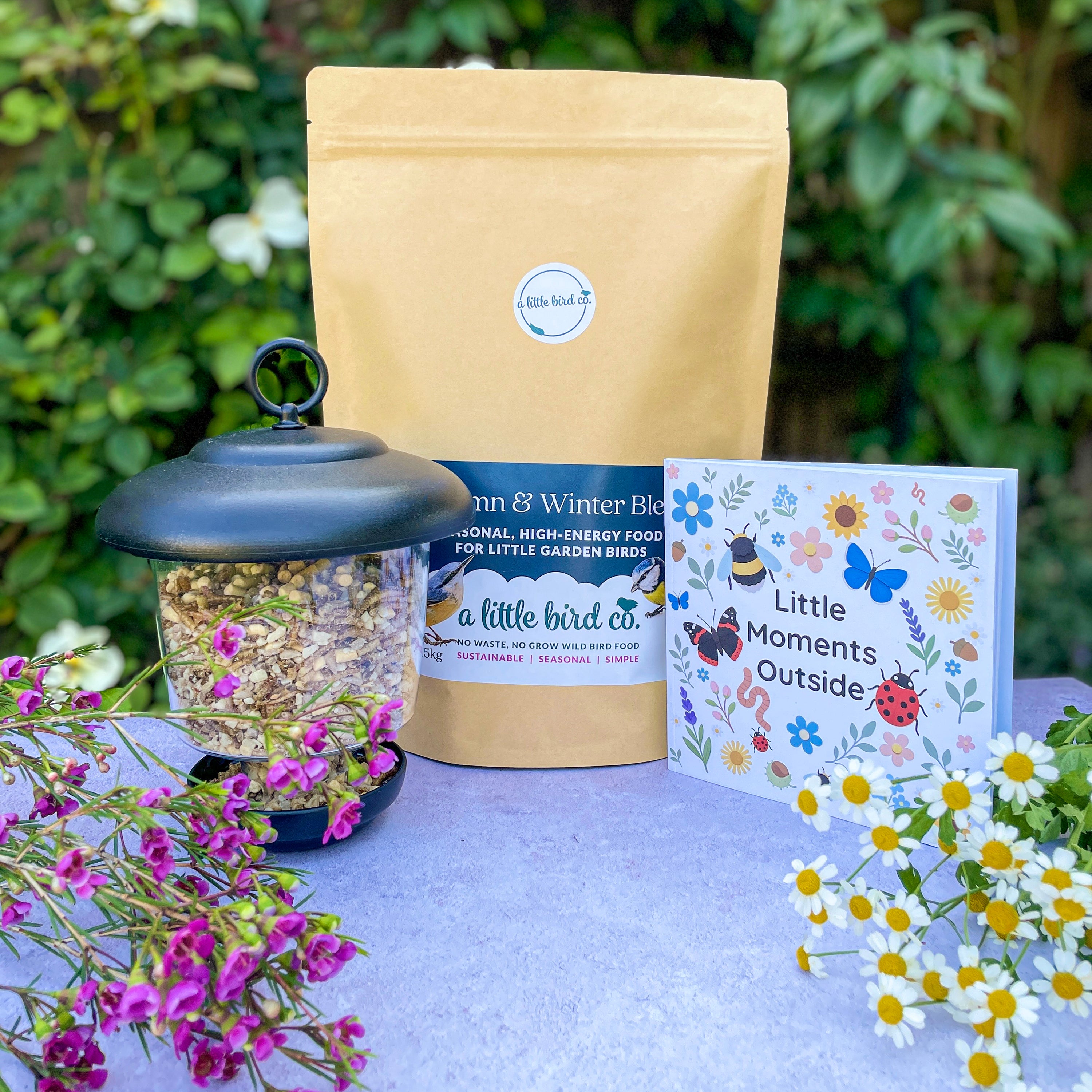 Bird feeder, bird food package, and card on a table with a garden background